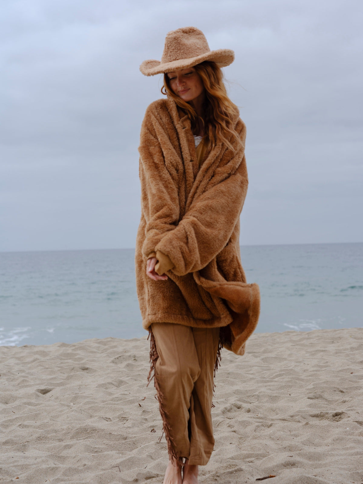 Model wearing the Camel Brown Long Papàsweater with a tan hat on the beach
