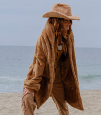 Model wearing the Camel Brown Long Papàsweater with a tan hat on the beach