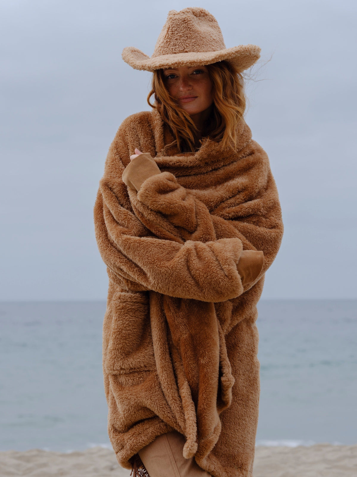 Model wearing the Camel Brown Long Papàsweater with a tan hat on the beach