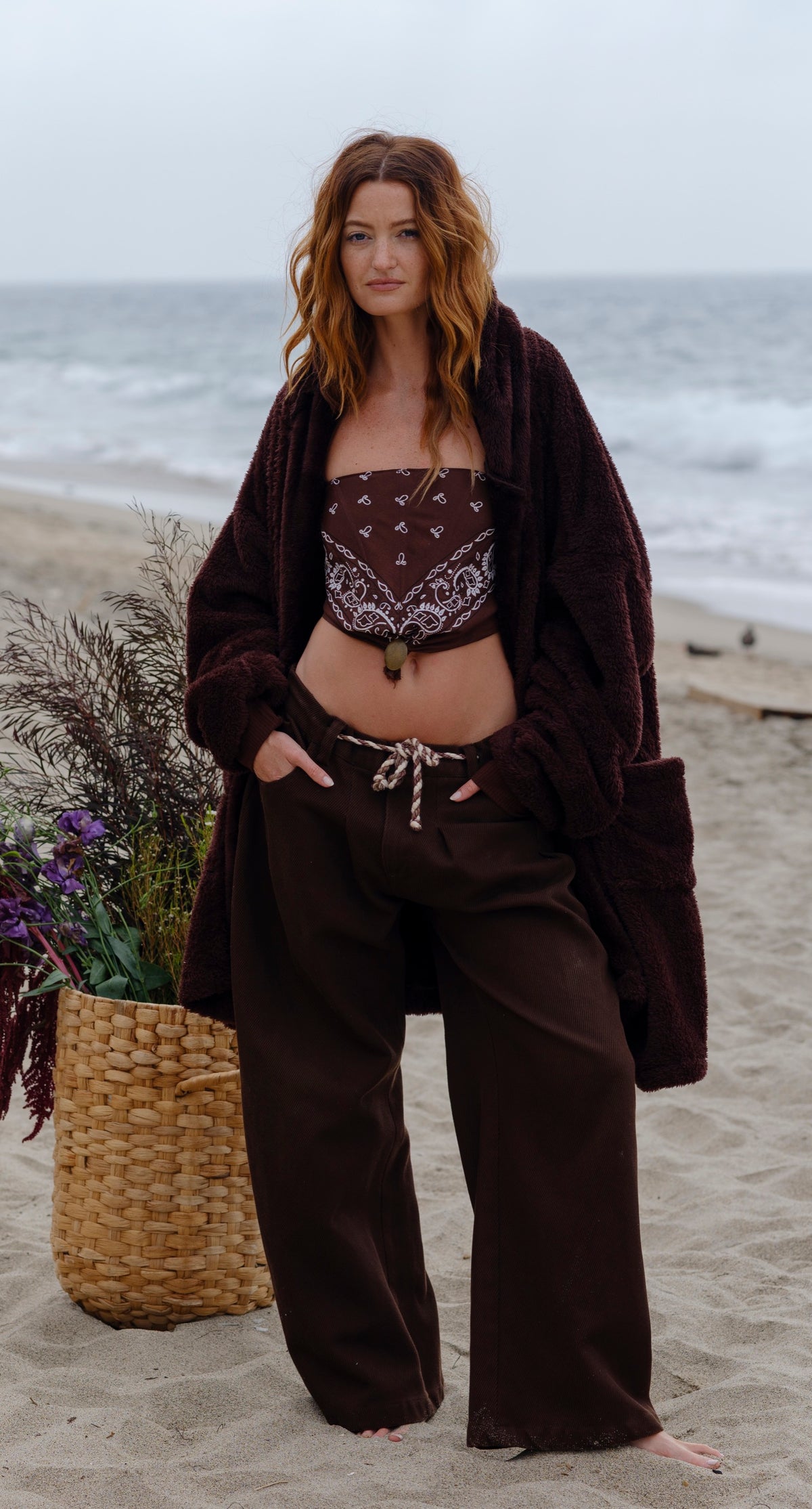 Model wearing the Dark Chocolate Long Papàsweater with brown trousers on the beach