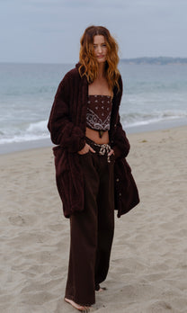 Model wearing the Dark Chocolate Long Papàsweater with brown trousers on the beach